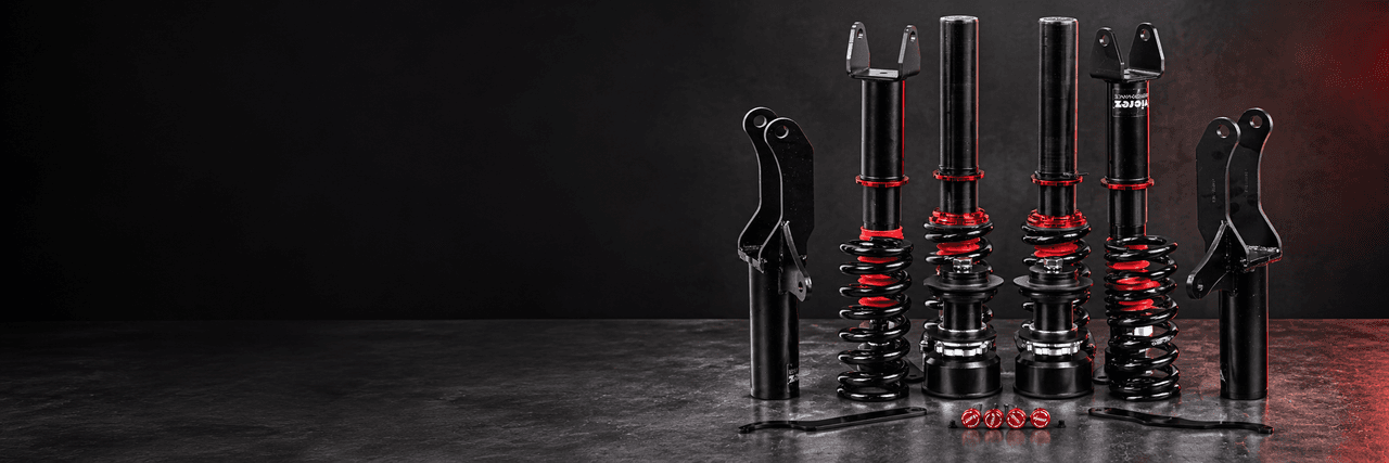 Black coilover suspension components with red adjustment collars on a studio workbench