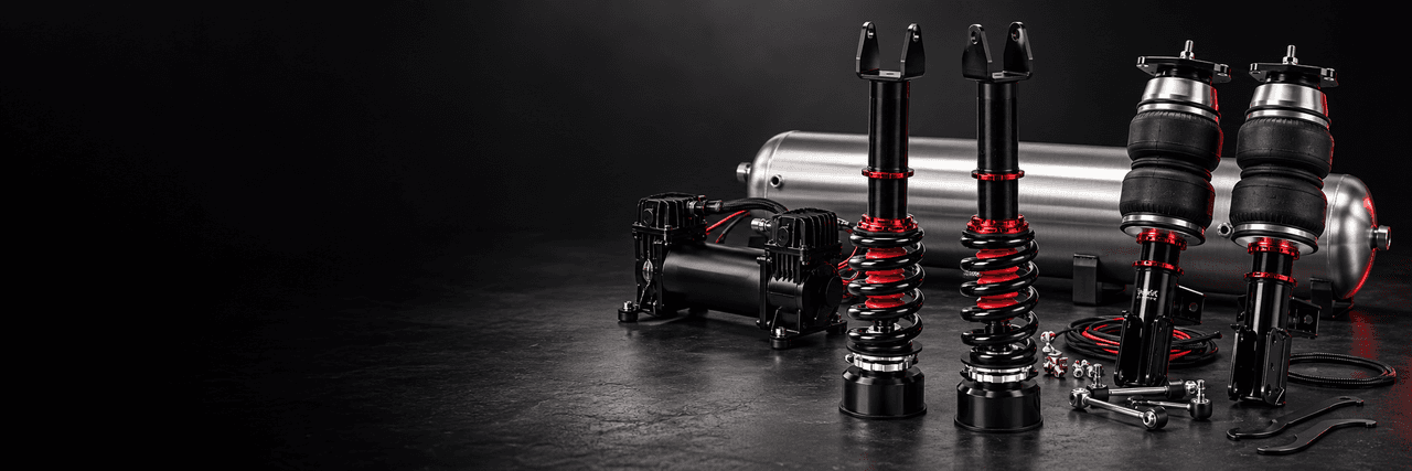 Black and red coilovers, air struts and air management components on a dark workbench