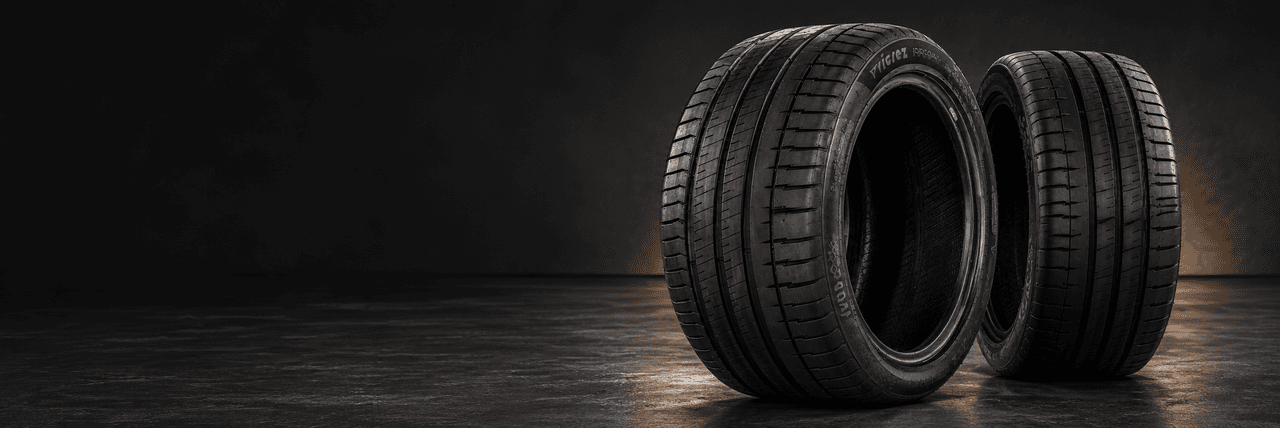 Two black performance tires showing the tread pattern and sidewalls in a dark studio