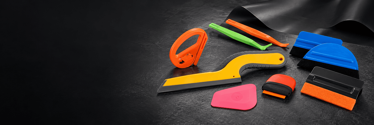 Colorful film applicators, felt-edge squeegees and a pocket cutter arranged on a dark workbench